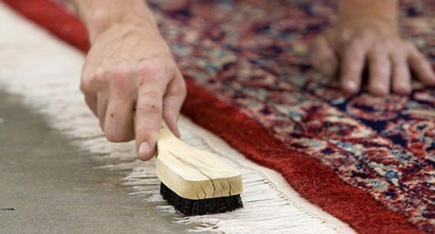 Hands working the worn edge of a handmade rug